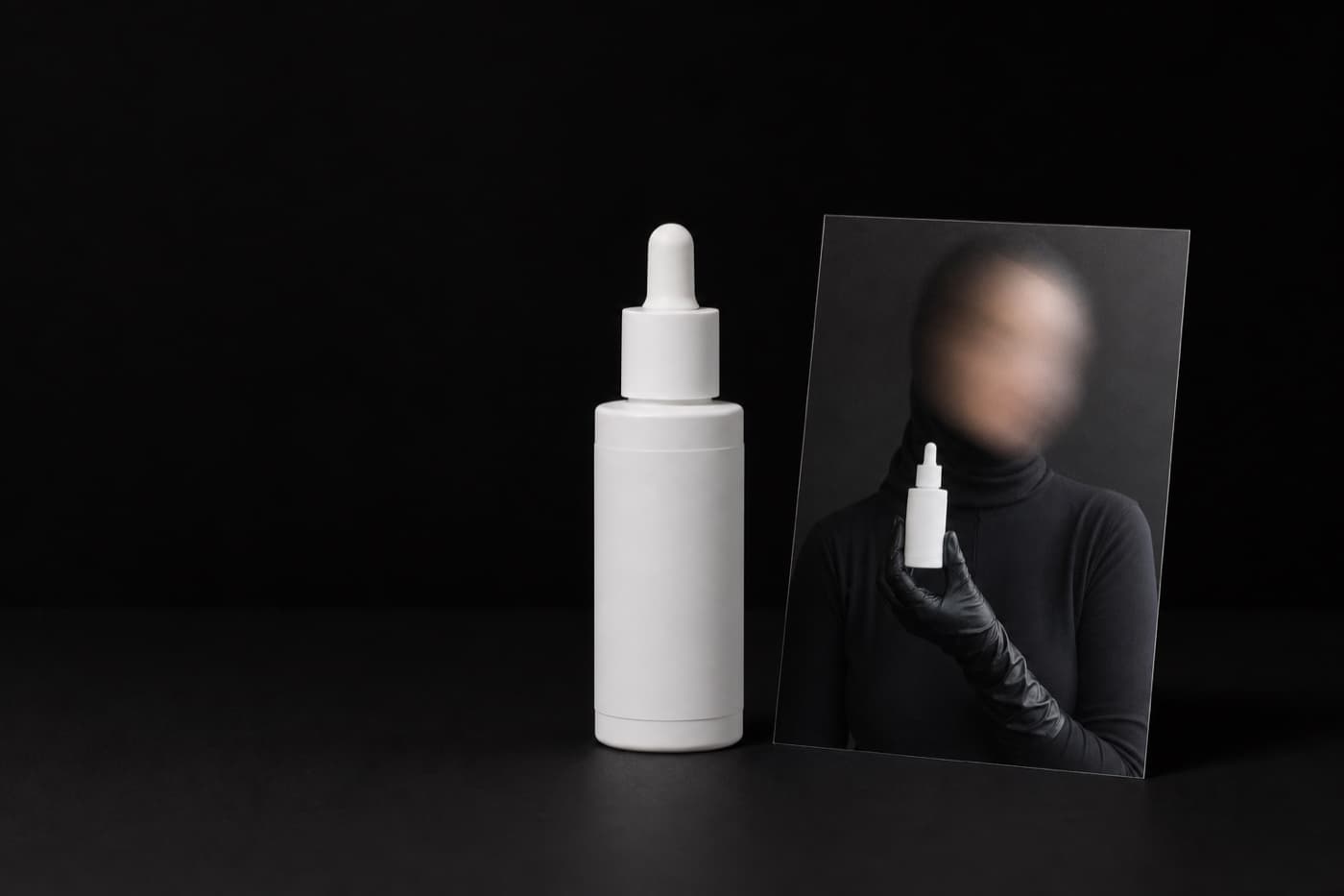 무광 흰 세럼 병 실물이 서 있고 옆에 같은 병을 든 모델의 인화 사진이 기대어 있다. 병의 형태와 라벨 위치가 같다