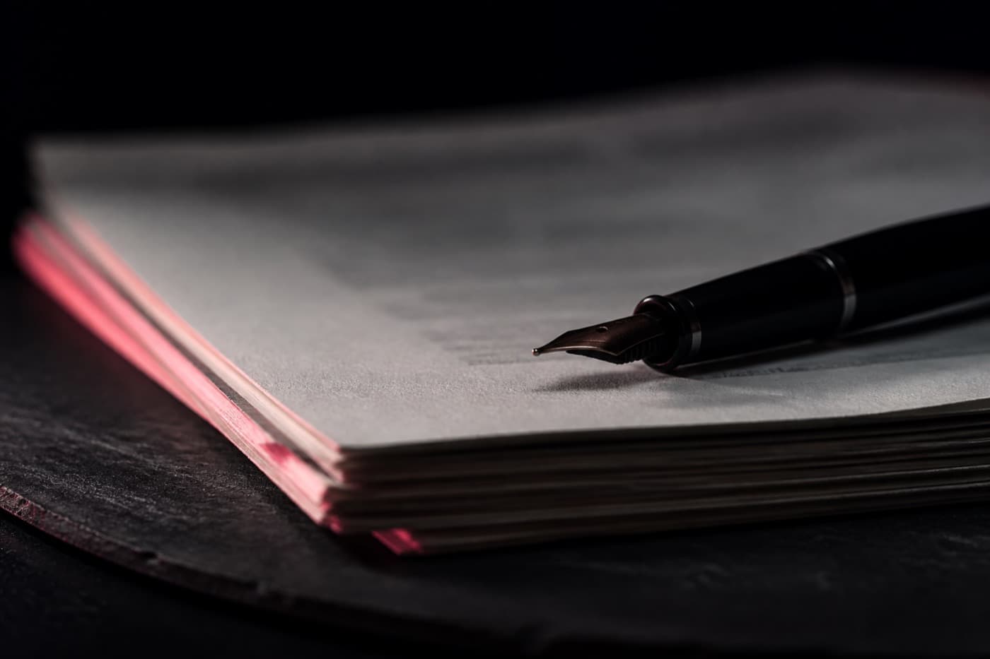 A stack of contracts and a fountain pen on a dark desk